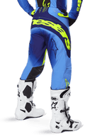 Alpinestars Techstar Melt Pants 2025, spodnie motocrossowe, żółty fluo niebieski, widok z tyłu z dużym żółtym brandingiem na siedzeniu i ciemnoniebieskimi akcentami, noszone z białymi butami Alpinestars Tech 10 i pasującą koszulką.
