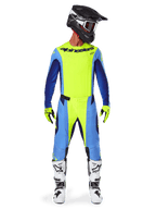 Alpinestars Techstar Melt Pants 2025, spodnie motocrossowe, żółty fluo i niebieski, noszone z dopasowaną koszulką, żółtymi rękawicami i biało-czarnymi butami, czarny kask z czerwonymi goglami, kompletny zestaw wyścigowy do jazdy off-road
