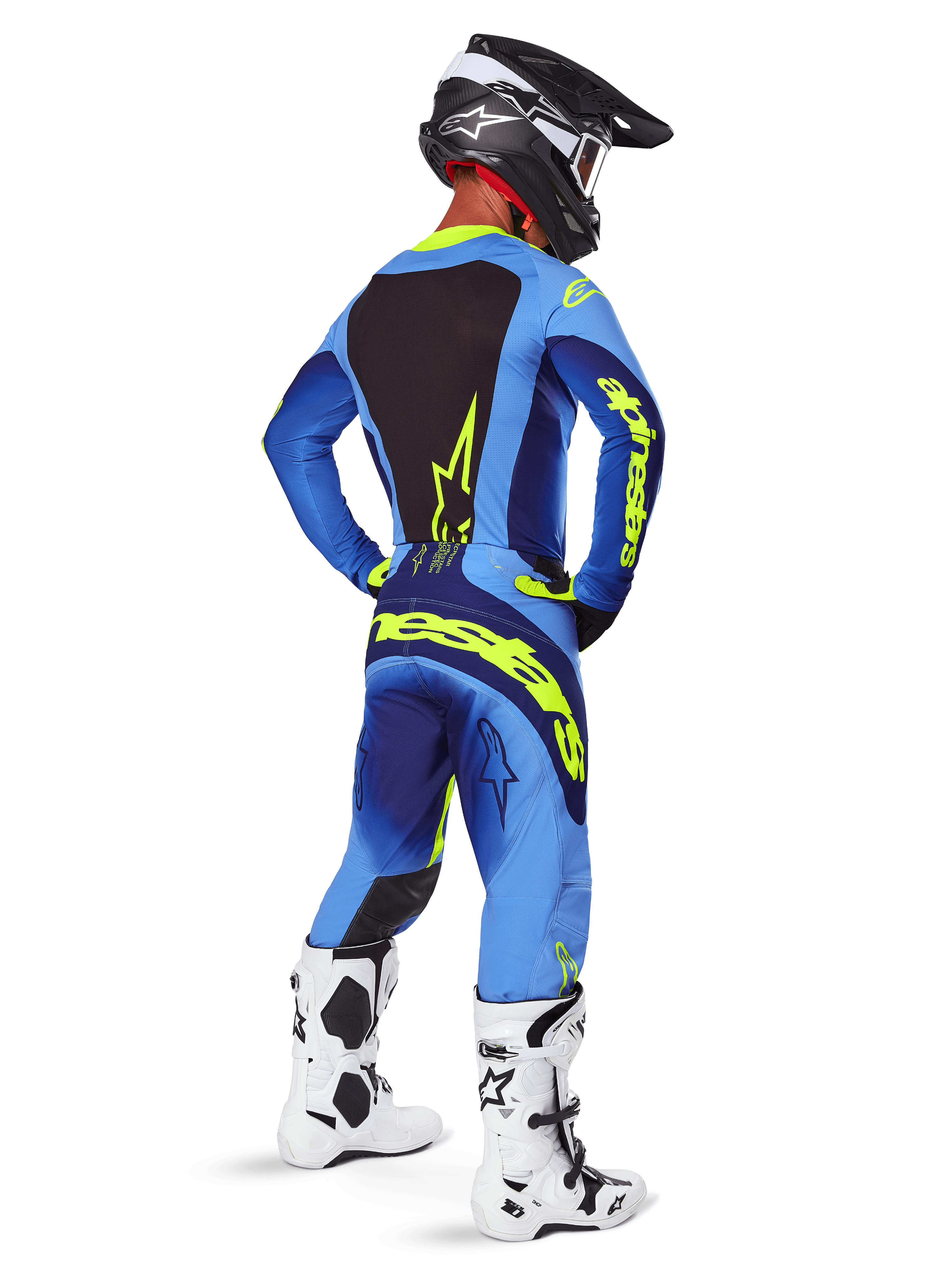 Spodnie Alpinestars Techstar Melt 2025, odzież motocrossowa, żółto-niebieskie (Yellow Fluo Blue), widok z tyłu na motocyklistę w dopasowanej niebieskiej koszulce z dużym żółtym logo, biało-czarne buty i czarny kask, skoordynowany strój wyścigowy do jazdy off-road