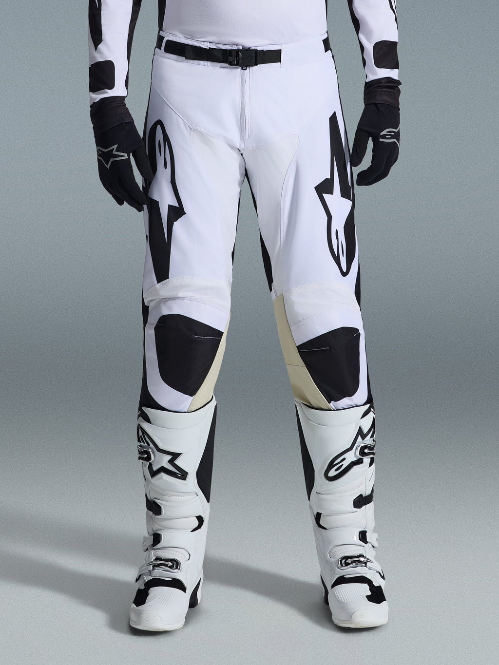 Alpinestars Racer Riway 2026, spodnie motocrossowe, biało-czarne, noszone z pasującymi biało-czarnymi butami motocrossowymi i czarnymi rękawicami, z wyrazistym czarnym logo Alpinestars na udach, techniczna konstrukcja do jazdy off-road