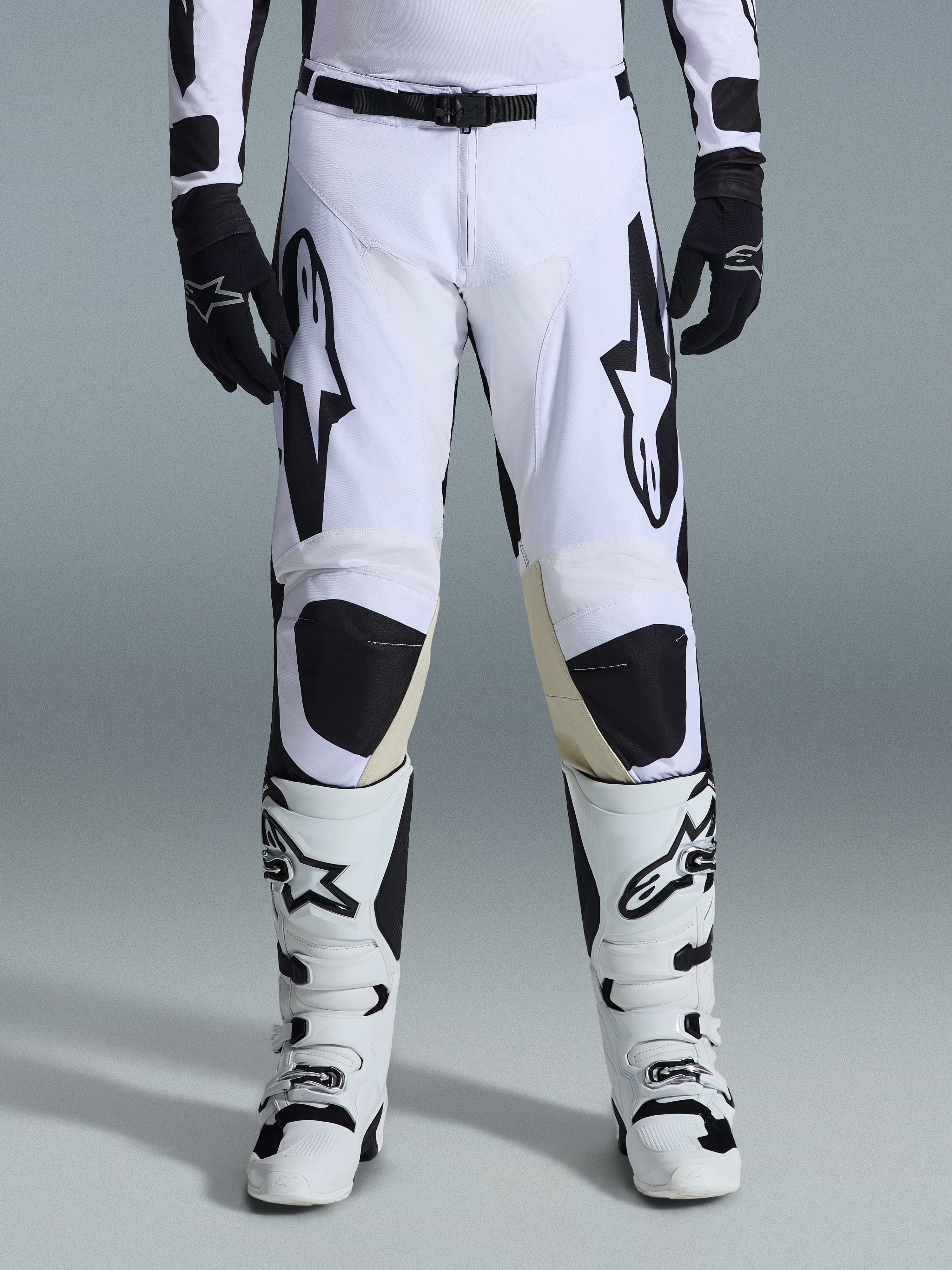 Alpinestars Racer Riway 2026, spodnie motocrossowe, biało-czarne, noszone z pasującymi biało-czarnymi butami motocrossowymi i czarnymi rękawicami, z wyrazistym czarnym logo Alpinestars na udach, techniczna konstrukcja do jazdy off-road