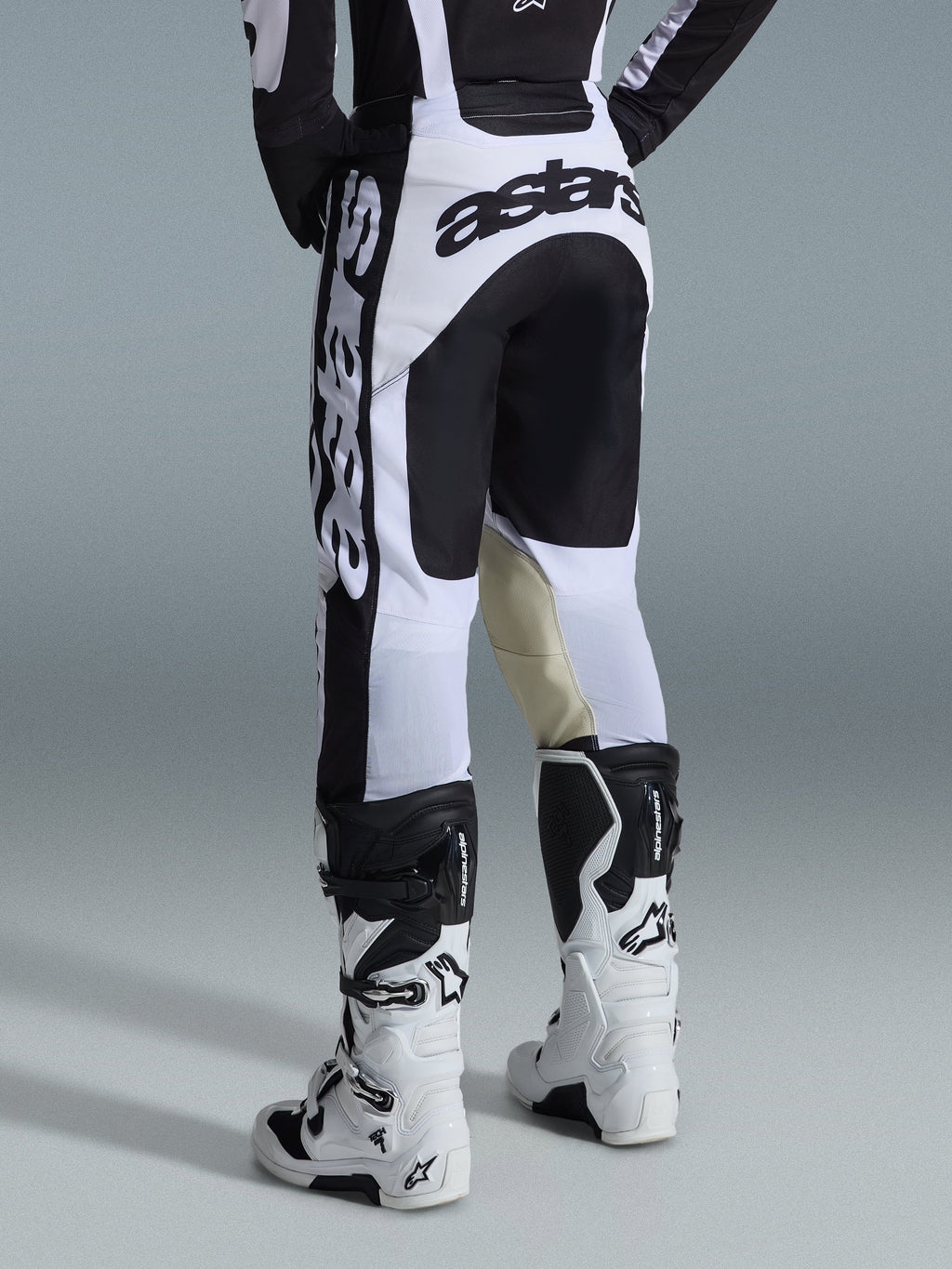 Alpinestars 2026 Racer Riway Pants, spodnie motocrossowe, biało-czarne, widok z tyłu ukazujący wyraźne czarne oznaczenia marki na siedzeniu i bokach, panele wewnętrzne kolan z beżowej koziej skóry, zestawione z pasującymi biało-czarnymi butami motocrossowymi