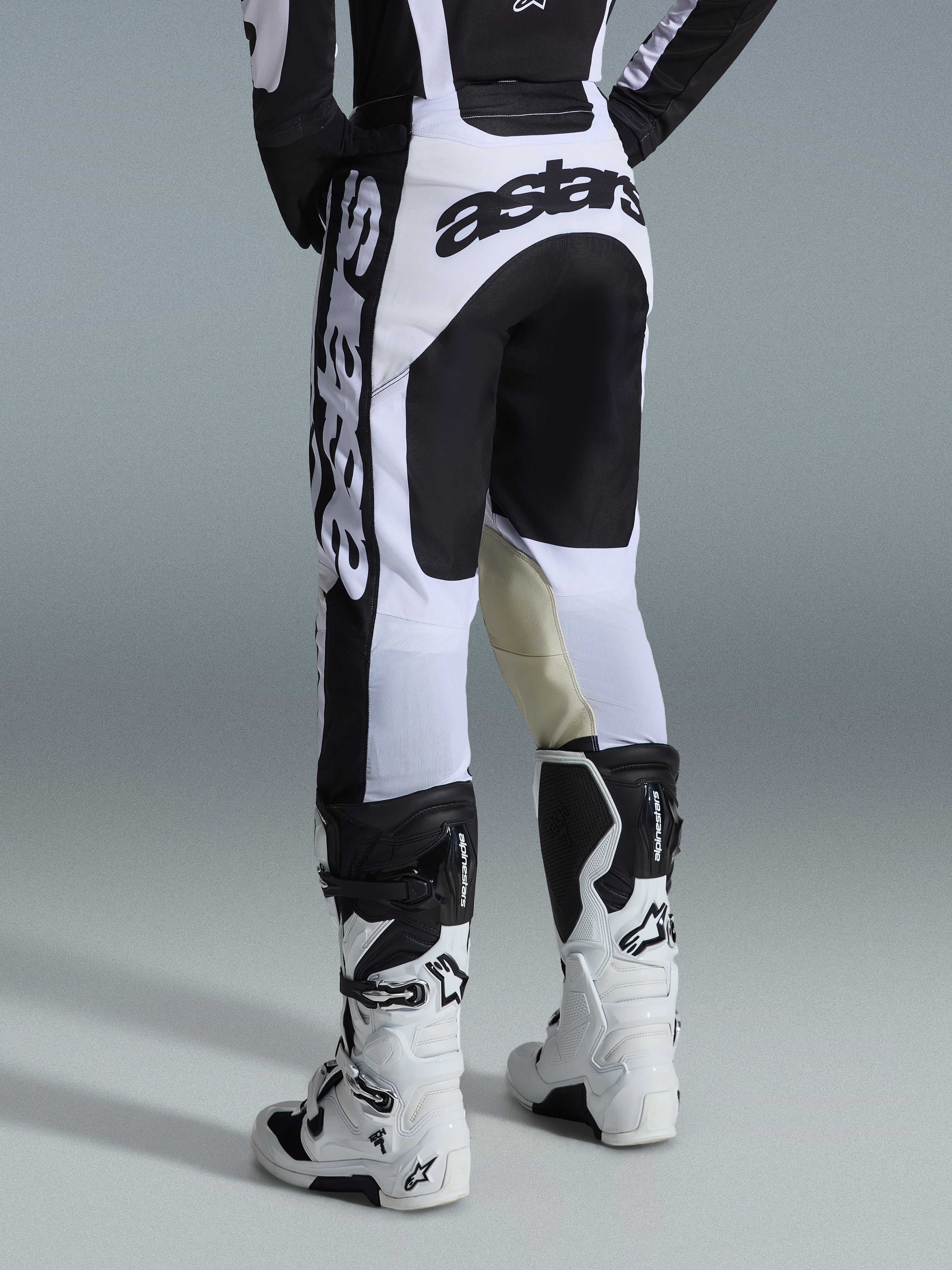 Alpinestars 2026 Racer Riway Pants, spodnie motocrossowe, biało-czarne, widok z tyłu ukazujący wyraźne czarne oznaczenia marki na siedzeniu i bokach, panele wewnętrzne kolan z beżowej koziej skóry, zestawione z pasującymi biało-czarnymi butami motocrossowymi