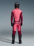 Zawodnik motocrossowy widziany od tyłu w koszulce Alpinestars 2026 Racer Riway i pasujących spodniach w kolorze Dark Red Coral, czarny kask, czarne rękawice i czarne buty, profesjonalny zestaw odzieży do jazdy terenowej