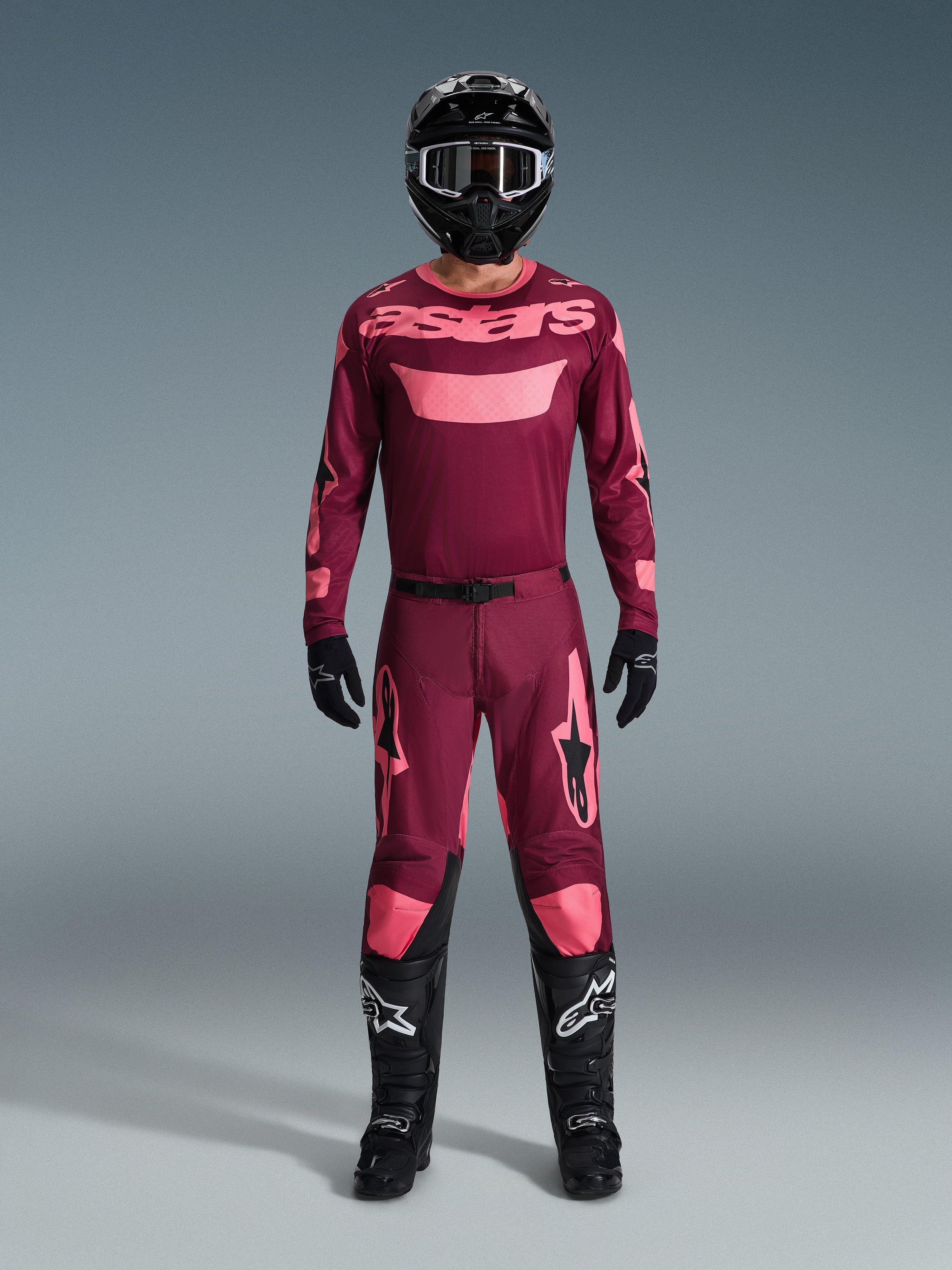 Zawodnik motocrossowy w pełnym stroju wyścigowym, koszulka 2026 Racer Riway w kolorze Dark Red Coral, pasujące ciemnoczerwone spodnie z koralowymi akcentami, czarny kask z białymi akcentami, czarne buty z białym logo i czarne rękawice, dopasowany strój do jazdy off-road