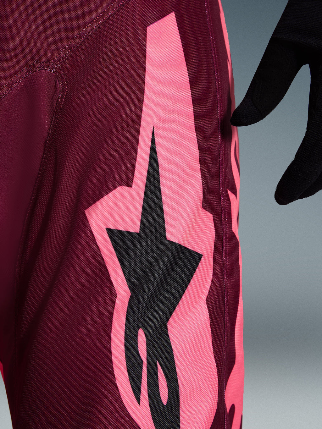 Alpinestars 2026 Racer Riway Pants, spodnie motocrossowe, kolor Dark Red Coral, widok z bliska na dużą koralowo-różową kanciastą grafikę i czarne logo gwiazdy, podkreślający wytrzymałą strukturę materiału polyfabric i sportowe szwy