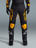 Alpinestars 2026 Racer Riway Pants, spodnie motocrossowe, żółto-czarne, noszone z czarnymi rękawicami motocrossowymi i czarnymi butami z białymi logo, z dużymi żółtymi logo Alpinestars na udach i żółtymi panelami na kolanach, wytrzymała konstrukcja zapewniająca wydajność w wyścigach terenowych