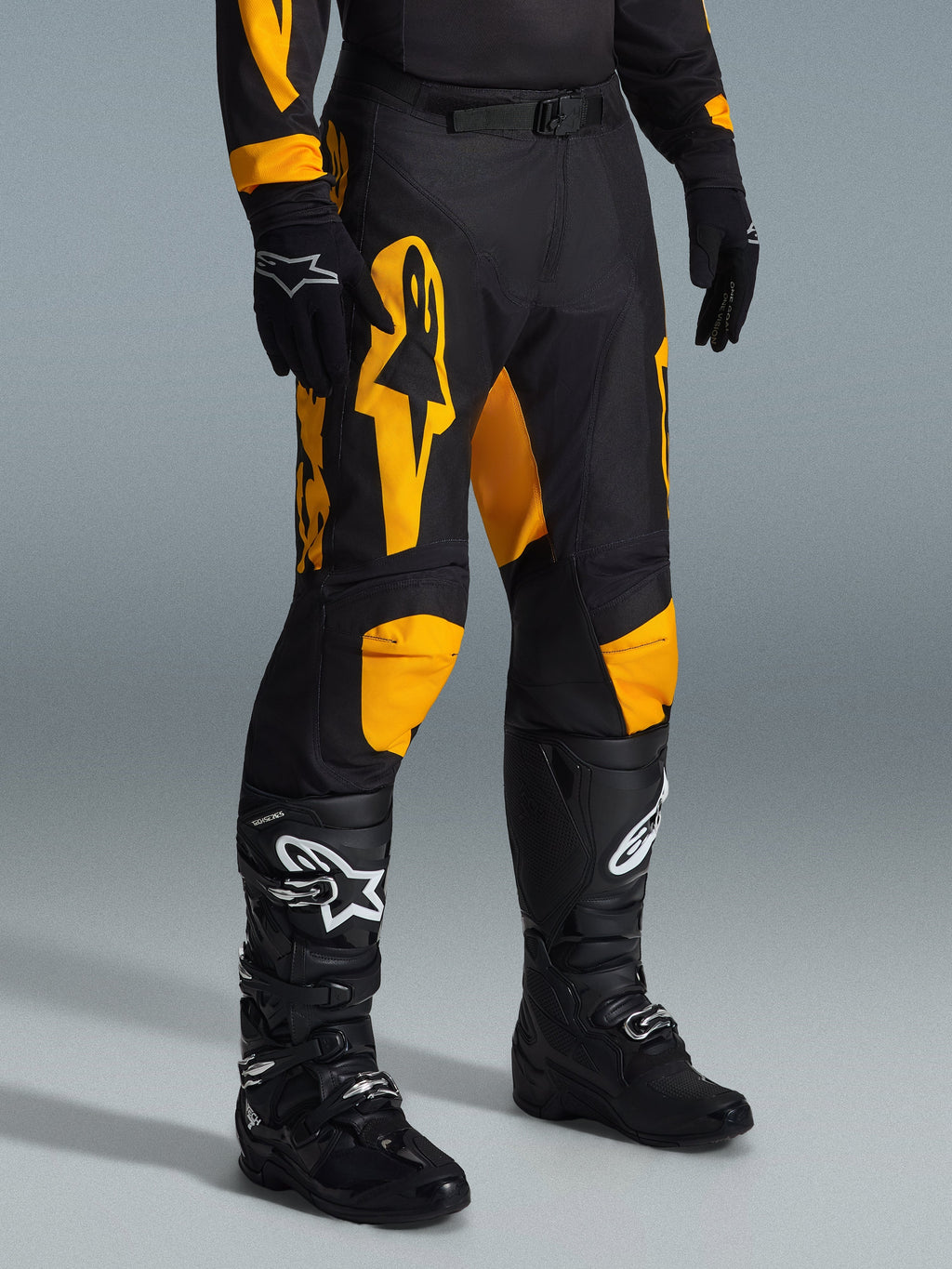 Alpinestars 2026 Racer Riway Pants, spodnie motocrossowe, żółto-czarne, noszone z czarnymi rękawicami i czarnymi butami motocrossowymi, z wyrazistym żółtym brandingiem Alpinestars i akcentami na kolanach na czarnej bazie, zaprojektowane do wyczynowej jazdy off-road