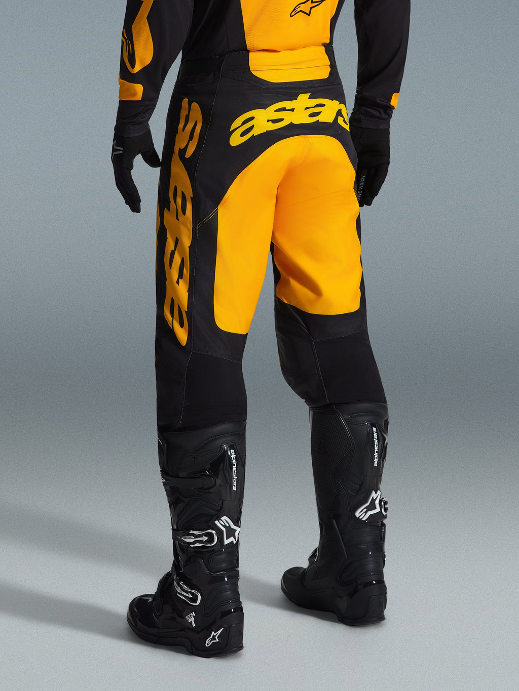 Alpinestars Racer Riway Pants 2026, spodnie motocrossowe, żółto-czarne, widok z tyłu ukazujący wyraźne żółte logo astars na siedzeniu i nogawce, w zestawieniu z czarnymi butami i rękawicami motocrossowymi