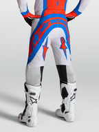 Alpinestars Spodnie Supertech Vesta, spodnie motocrossowe pro-level, białe, niebieskie i czerwone, z perforowaną tkaniną rip-stop, na modelu z butami Tech 10