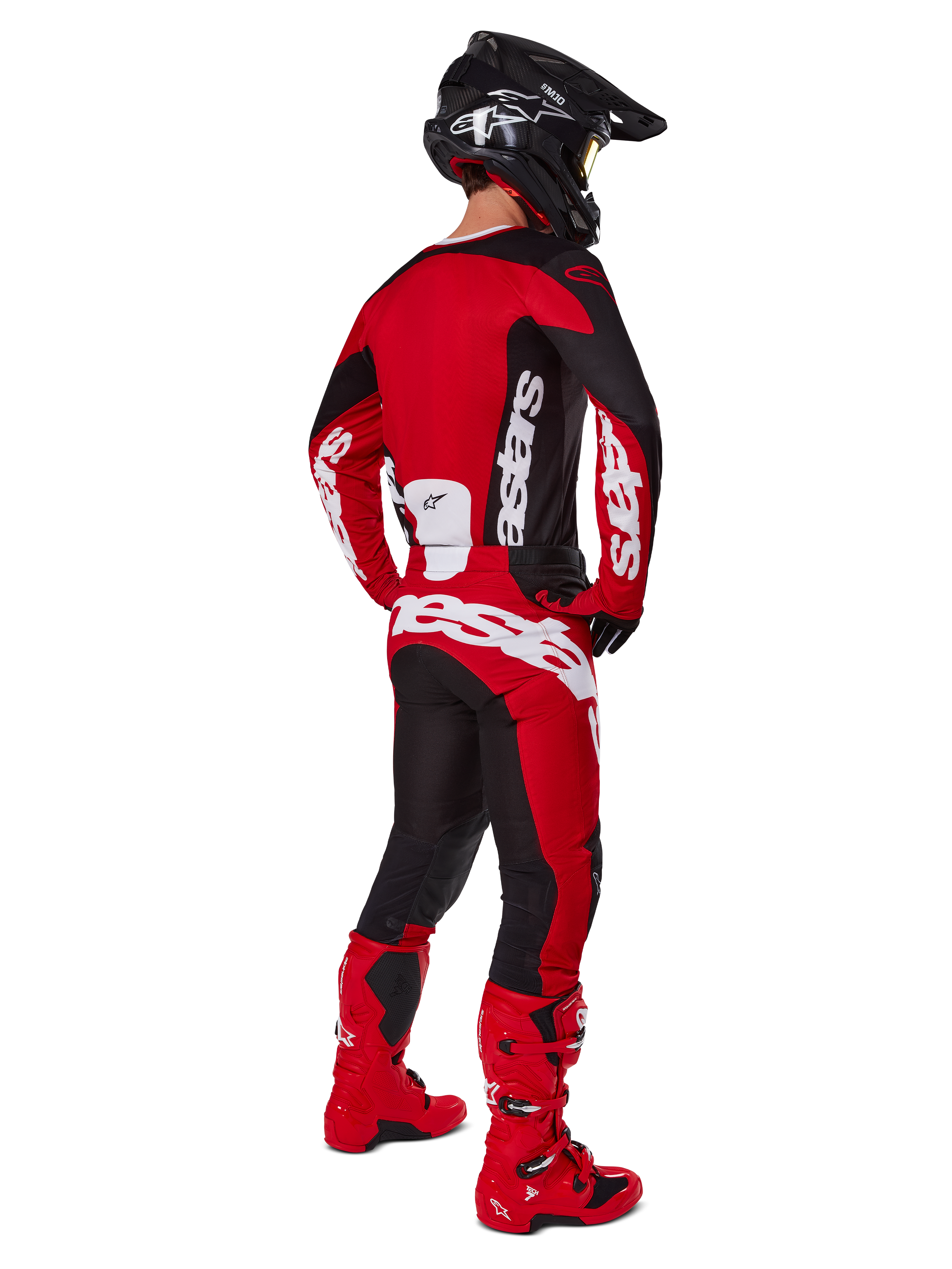 Zestaw Alpinestars 2025 Racer Veil, motocyklista motocrossowy widziany od tyłu w czerwonej koszulce z czarnymi panelami i białym logo, pasujące czerwono-czarne spodnie z dużymi białymi oznaczeniami marki, czerwone buty i czarny kask, kompletny strój wyścigowy off-road