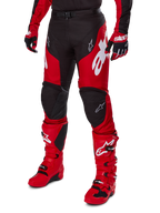 Motocyklista motocrossowy w zestawie Alpinestars 2025 Racer Veil, czerwono-czarna koszulka i spodnie z białym logo, dopasowane rękawice i jaskrawoczerwone buty motocrossowe, profesjonalna odzież do jazdy terenowej.
