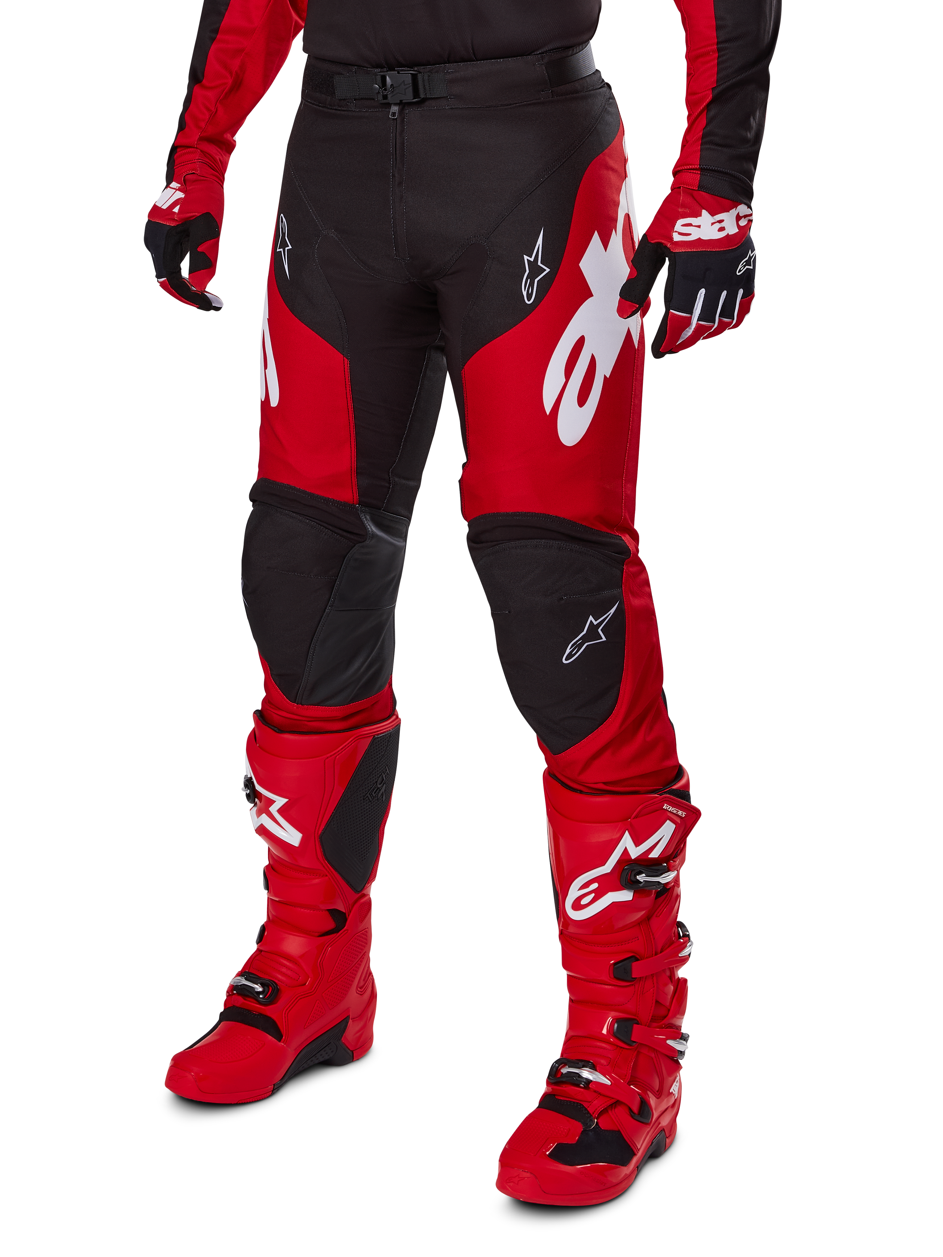 Motocyklista motocrossowy w zestawie Alpinestars 2025 Racer Veil, czerwono-czarna koszulka i spodnie z białym logo, dopasowane rękawice i jaskrawoczerwone buty motocrossowe, profesjonalna odzież do jazdy terenowej.