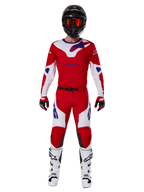 Alpinestars 2025 Racer Veil Pants i kompletny zestaw odzieży motocrossowej, jaskrawoczerwony i biały z niebieskimi akcentami, z dopasowaną koszulką, czarnym kaskiem z pomarańczowymi goglami, biało-czarnymi butami i czerwonymi rękawicami, spójny, wyczynowy wygląd do wyścigów terenowych