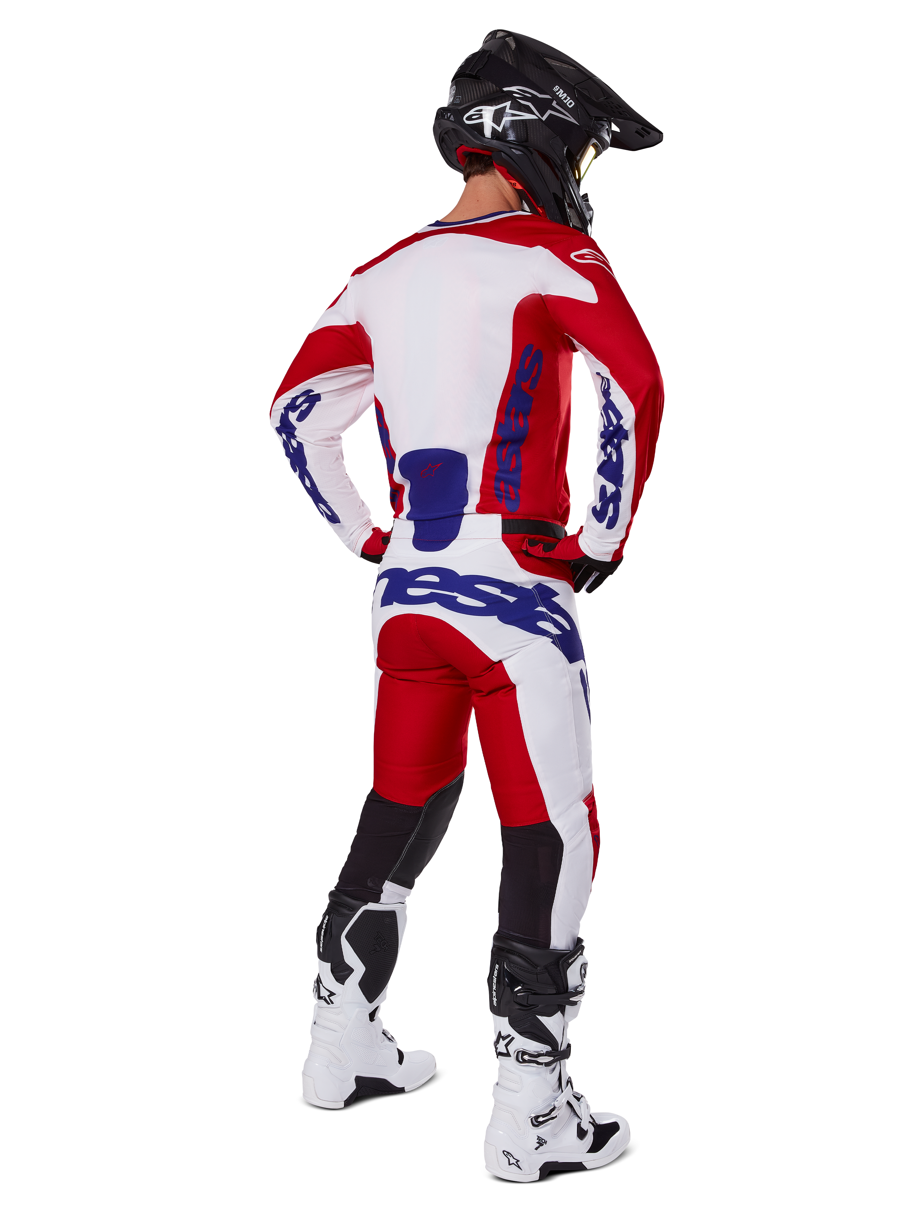 Alpinestars Racer Veil Pants 2025, spodnie motocrossowe, jaskrawoczerwone i białe z niebieskimi akcentami, widok od tyłu na motocyklistę w pełnym stroju, wyraźne logo Alpinestars, oddychające panele na dolnej części nogawek, białe buty i czarny kask
