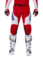 Alpinestars 2025 Racer Veil Pants, spodnie motocrossowe, jaskrawoczerwone i białe, zestawione z czerwonymi rękawicami i białymi butami, niebieskie logo na udach, czarny pas w talii, ergonomiczny sportowy krój