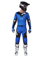 Alpinestars 2025 Racer Veil Pants, spodnie motocrossowe, niebiesko-czarne, kompletny strój wyścigowy z dopasowaną niebiesko-czarną koszulką, czarno-białym kaskiem, niebieskimi rękawicami i białymi butami, wyraźne logo, ergonomiczna konstrukcja do jazdy terenowej