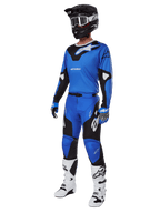 Zawodnik motocrossowy w kompletnym stroju wyścigowym, spodnie Alpinestars 2025 Racer Veil w kolorze niebiesko-czarnym, dopasowana niebieska koszulka z białymi akcentami, czarny kask z białymi goglami, biało-czarne buty i niebieskie rękawice, spójny zestaw do jazdy terenowej