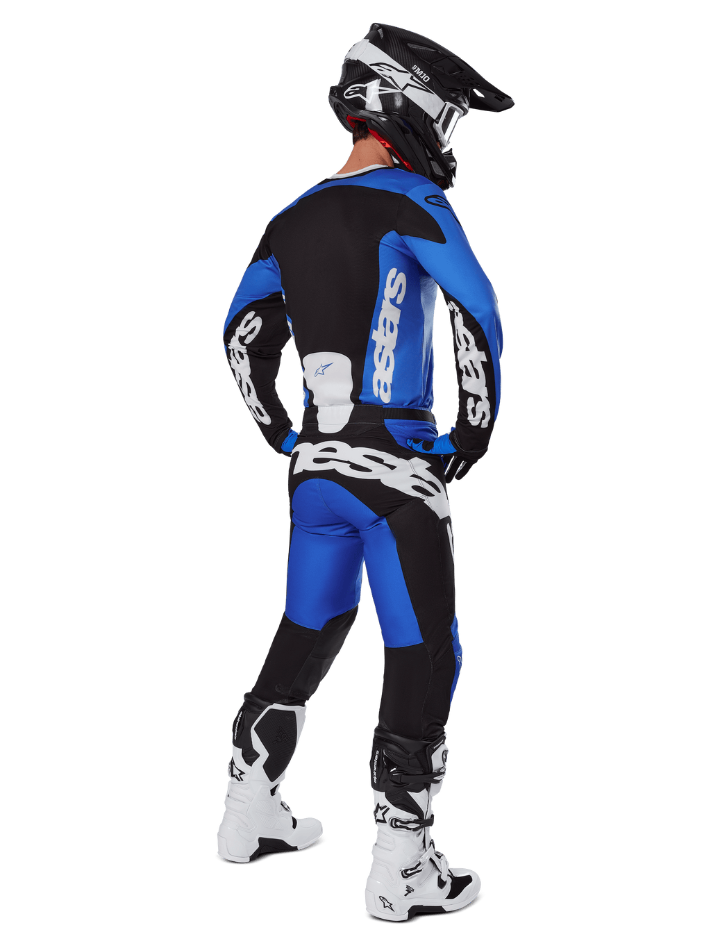 Motocyklista motocrossowy widziany od tyłu, ubrany w spodnie Alpinestars 2025 Racer Veil w kolorze niebiesko-czarnym, pasującą koszulkę z długim rękawem z białym brandingiem, biało-czarne buty Tech 7 oraz czarny kask SM10, pełny zestaw wyścigowy off-road