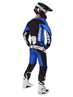 Motocyklista motocrossowy widziany od tyłu, ubrany w spodnie Alpinestars 2025 Racer Veil w kolorze niebiesko-czarnym, pasującą koszulkę z długim rękawem z białym brandingiem, biało-czarne buty Tech 7 oraz czarny kask SM10, pełny zestaw wyścigowy off-road