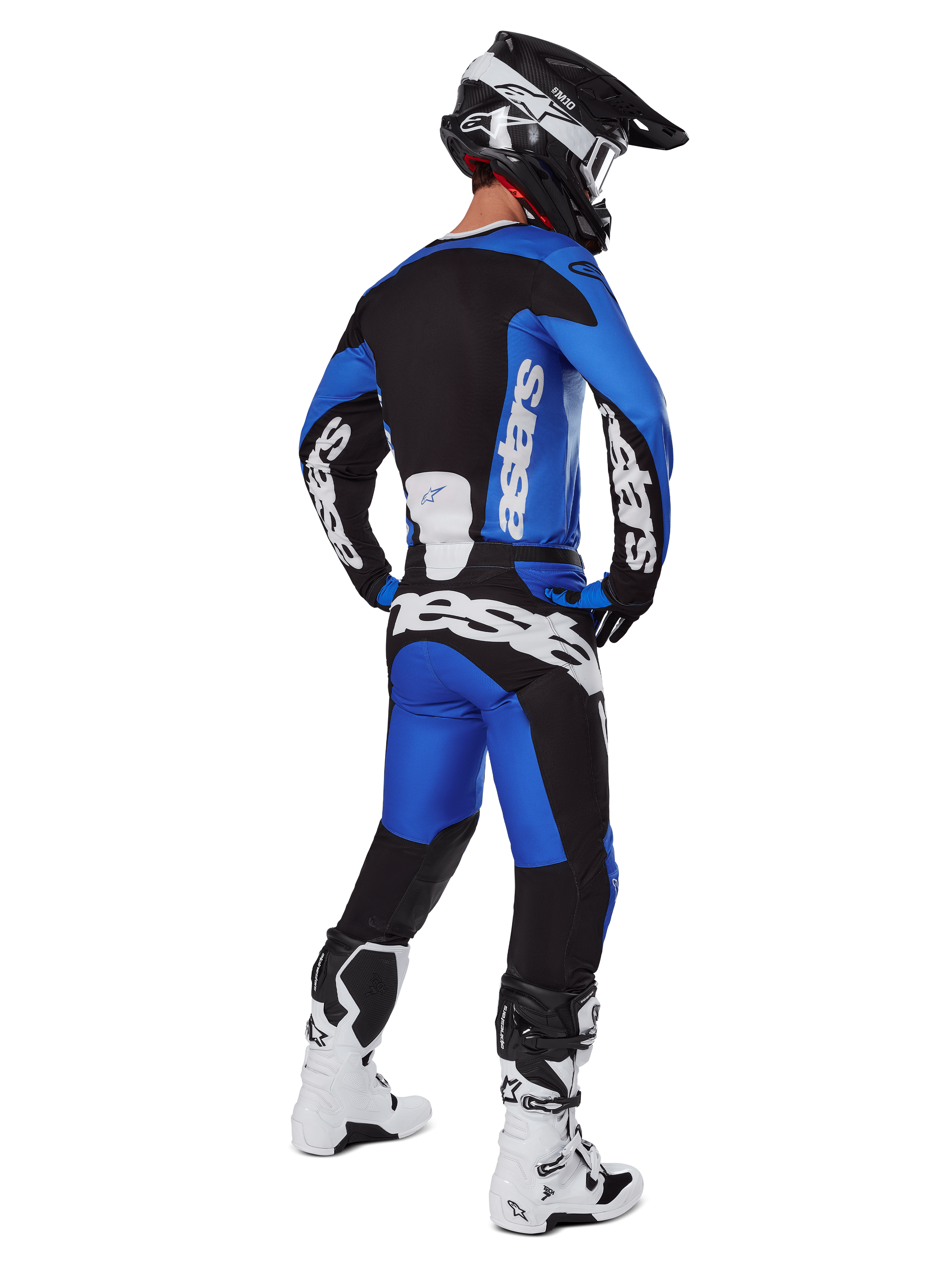 Motocyklista motocrossowy widziany od tyłu, ubrany w spodnie Alpinestars 2025 Racer Veil w kolorze niebiesko-czarnym, pasującą koszulkę z długim rękawem z białym brandingiem, biało-czarne buty Tech 7 oraz czarny kask SM10, pełny zestaw wyścigowy off-road