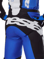 Alpinestars Racer Veil Pants 2025, spodnie motocrossowe, niebiesko-czarne, zbliżenie na tył z dużym białym napisem Alpinestars na czarnym panelu siedziska, noszone z dopasowanym niebiesko-czarnym osprzętem dla spójnego wyglądu terenowego