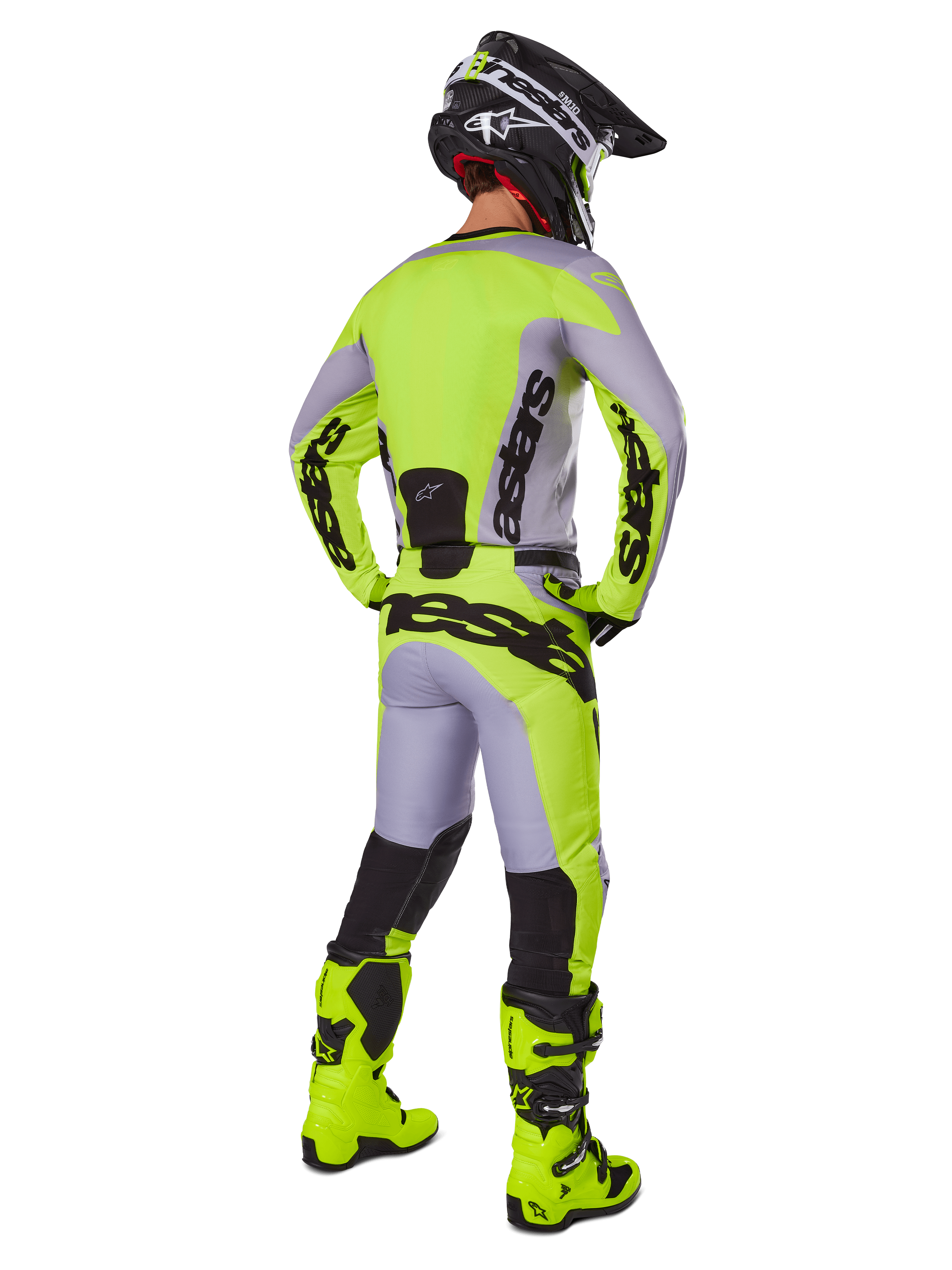 Alpinestars 2025 Racer Veil Pants, spodnie motocrossowe, szare i żółte fluorescencyjne, widok z tyłu zawodnika w pełnym stroju, pasująca bluza i żółte neonowe buty, wyraźne czarne logo, techniczny zestaw do wyścigów terenowych