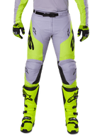 Alpinestars 2025 Racer Veil Pants, spodnie motocrossowe, szare i żółte fluo, noszone z pasującymi neonowożółtymi butami i rękawicami, czarne logo Alpinestars, ergonomiczna konstrukcja do jazdy terenowej