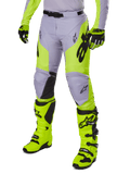 Alpinestars 2025 Racer Veil Pants, spodnie motocrossowe, szare i neonowe żółte fluo, z czarnym logo gwiazdy i regulowanym pasem, widoczne z dopasowanymi butami i rękawicami motocrossowymi, ergonomiczna konstrukcja do jazdy terenowej