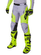 Alpinestars 2025 Racer Veil Pants, spodnie motocrossowe, szare i neonowe żółte fluo, z czarnym logo gwiazdy i regulowanym pasem, widoczne z dopasowanymi butami i rękawicami motocrossowymi, ergonomiczna konstrukcja do jazdy terenowej