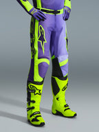 Alpinestars 2026 Racer Portl Pants, spodnie motocrossowe w kolorze fioletowym i żółtym fluo, noszone przez motocyklistę z pasującymi żółtymi neonowymi butami i fioletowymi rękawicami, z wyraźnym logo Alpinestars i ergonomiczną konstrukcją zapewniającą wydajność w terenie