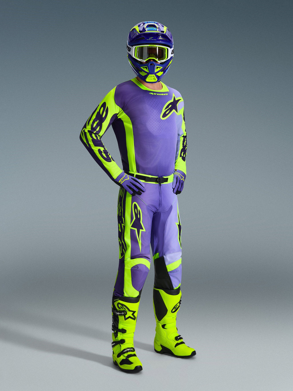 Zawodnik motocrossowy w stroju Alpinestars 2026 Racer Portl, fioletowo-żółta koszulka i spodnie fluo, neonowożółte buty, fioletowe rękawice i pasujący kask, kompletny zestaw wyścigowy do jazdy off-road