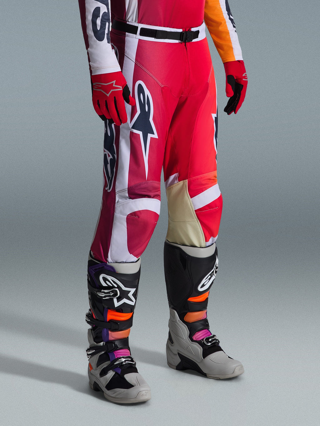 Spodnie Alpinestars 2026 Racer Portl, spodnie motocrossowe, czerwone, jasnoszare i ciemnoszare, noszone z pasującymi czerwonymi rękawicami i wielokolorowymi butami motocrossowymi, z wyraźnymi logotypami Alpinestars i wzmocnionymi panelami do wyścigów terenowych.