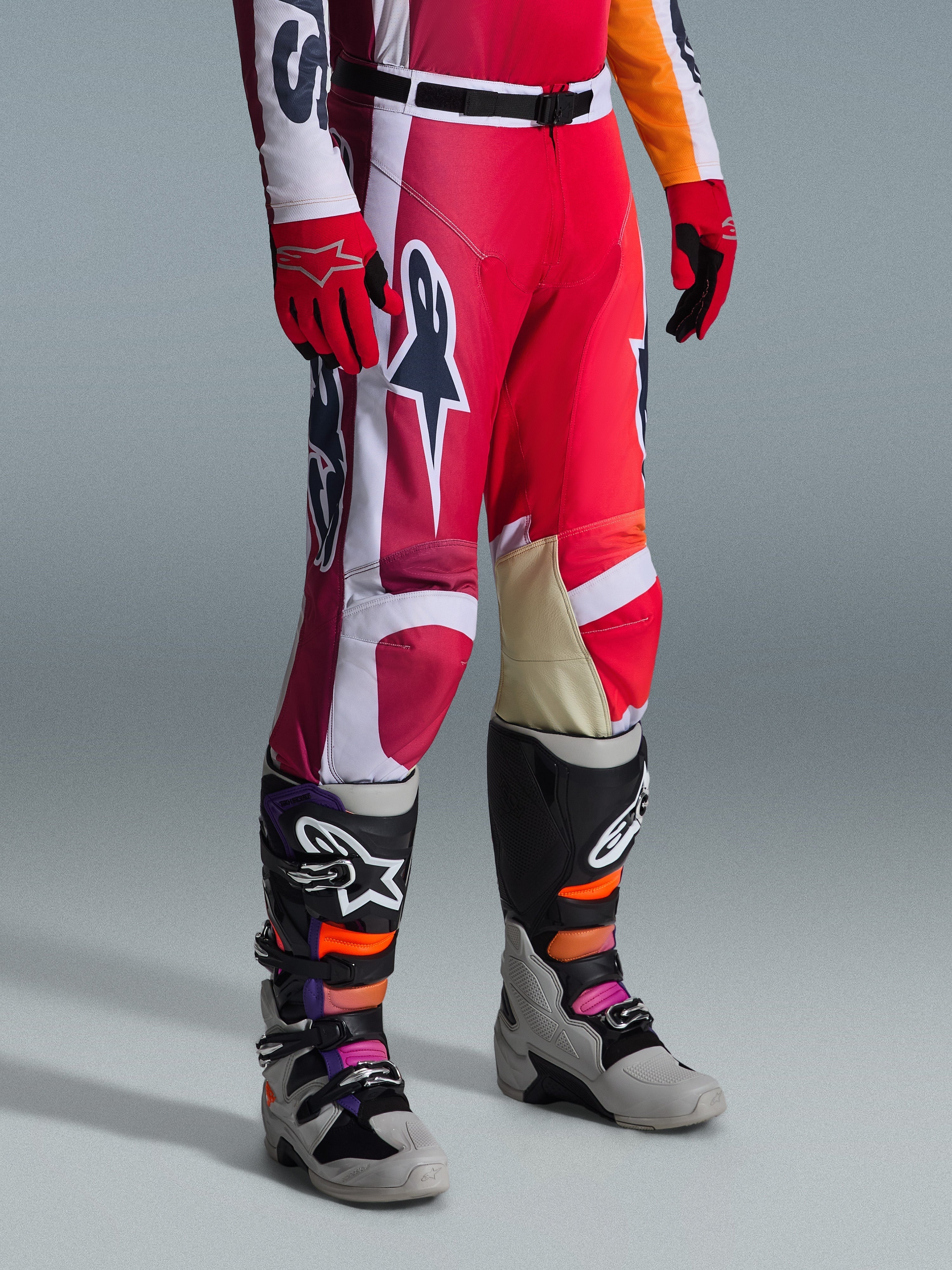 Spodnie Alpinestars 2026 Racer Portl, spodnie motocrossowe, czerwone, jasnoszare i ciemnoszare, noszone z pasującymi czerwonymi rękawicami i wielokolorowymi butami motocrossowymi, z wyraźnymi logotypami Alpinestars i wzmocnionymi panelami do wyścigów terenowych.