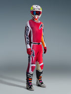 Spodnie Alpinestars 2026 Racer Portl, spodnie motocrossowe, czerwone, jasnoszare i ciemnoszare, noszone jako element pełnego stroju wyścigowego z pasującą koszulką, czerwonymi rękawicami, kolorowym kaskiem z niebieskimi goglami oraz szarymi butami, wytrzymała konstrukcja do jazdy motocrossowej.