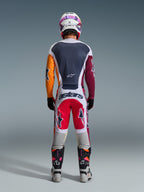 Motocyklista motocrossowy widziany od tyłu, ubrany w spodnie Racer Portl 2026 w kolorach czerwonym, jasnoszarym i ciemnoszarym, z napisem „astars” na siedzeniu, zestawione z wielokolorową koszulką, białym kaskiem i technicznymi butami wyścigowymi.