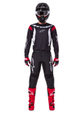 Alpinestars 2025 Fluid Haul Gear Set, zawodnik motocrossowy w pełnym stroju wyścigowym, czarna koszulka z czerwonymi akcentami na ramionach i białym logo, czarne spodnie z białym logo gwiazdy, jaskrawoczerwone buty, czerwono-czarne rękawice, czarny kask z białymi goglami, spójny wyczynowy styl off-road
