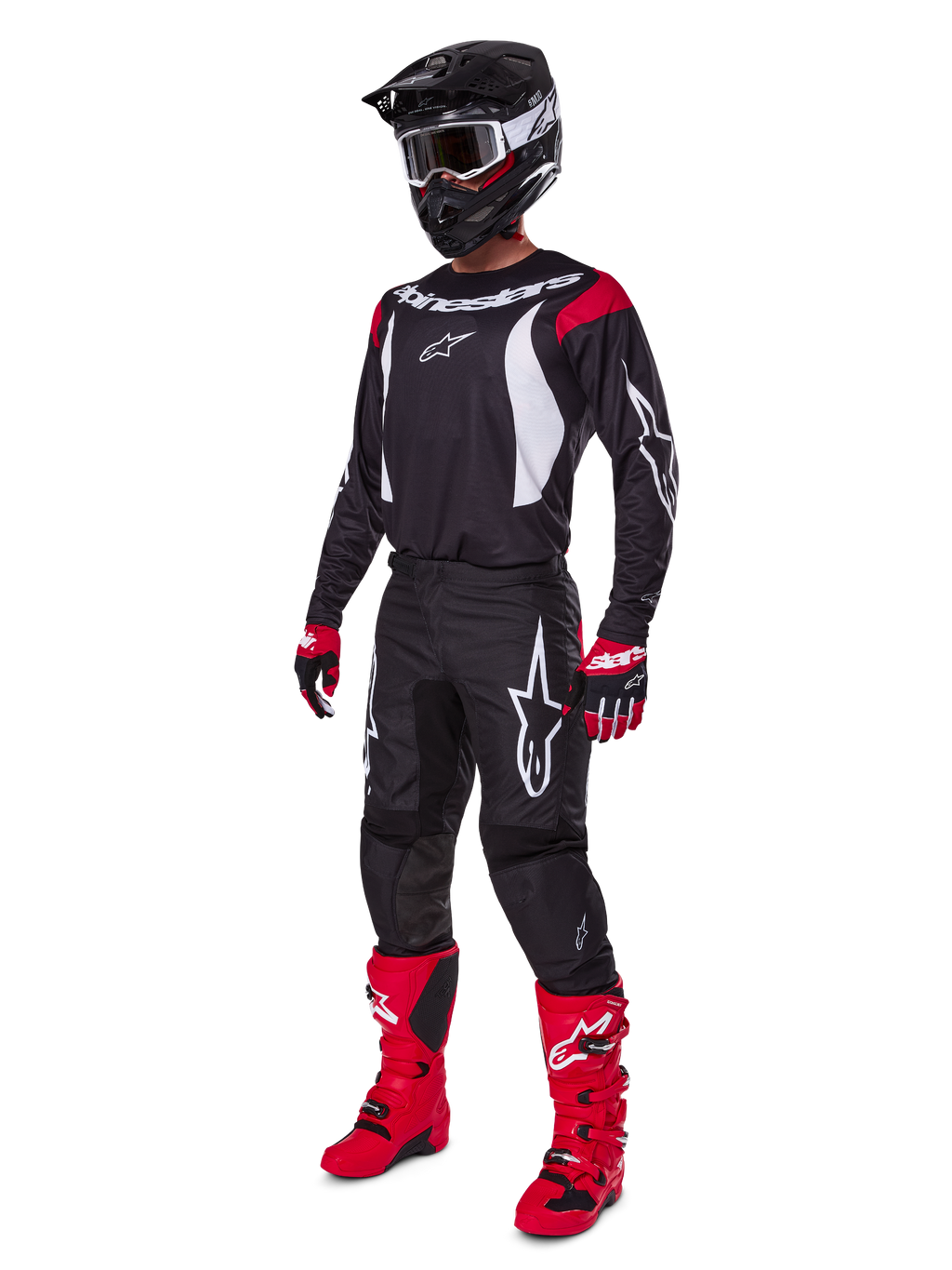 Motocyklista motocrossowy w kompletnym zestawie Alpinestars 2025 Fluid Haul, czarna koszulka z czerwonymi i białymi akcentami, czarne spodnie z białym logo, jaskrawoczerwone buty, czerwono-czarne rękawice, czarny kask z goglami, dopasowany zestaw odzieży off-road