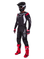 Motocyklista motocrossowy w kompletnym zestawie Alpinestars 2025 Fluid Haul, czarna koszulka z czerwonymi i białymi akcentami, czarne spodnie z białym logo, jaskrawoczerwone buty, czerwono-czarne rękawice, czarny kask z goglami, dopasowany zestaw odzieży off-road