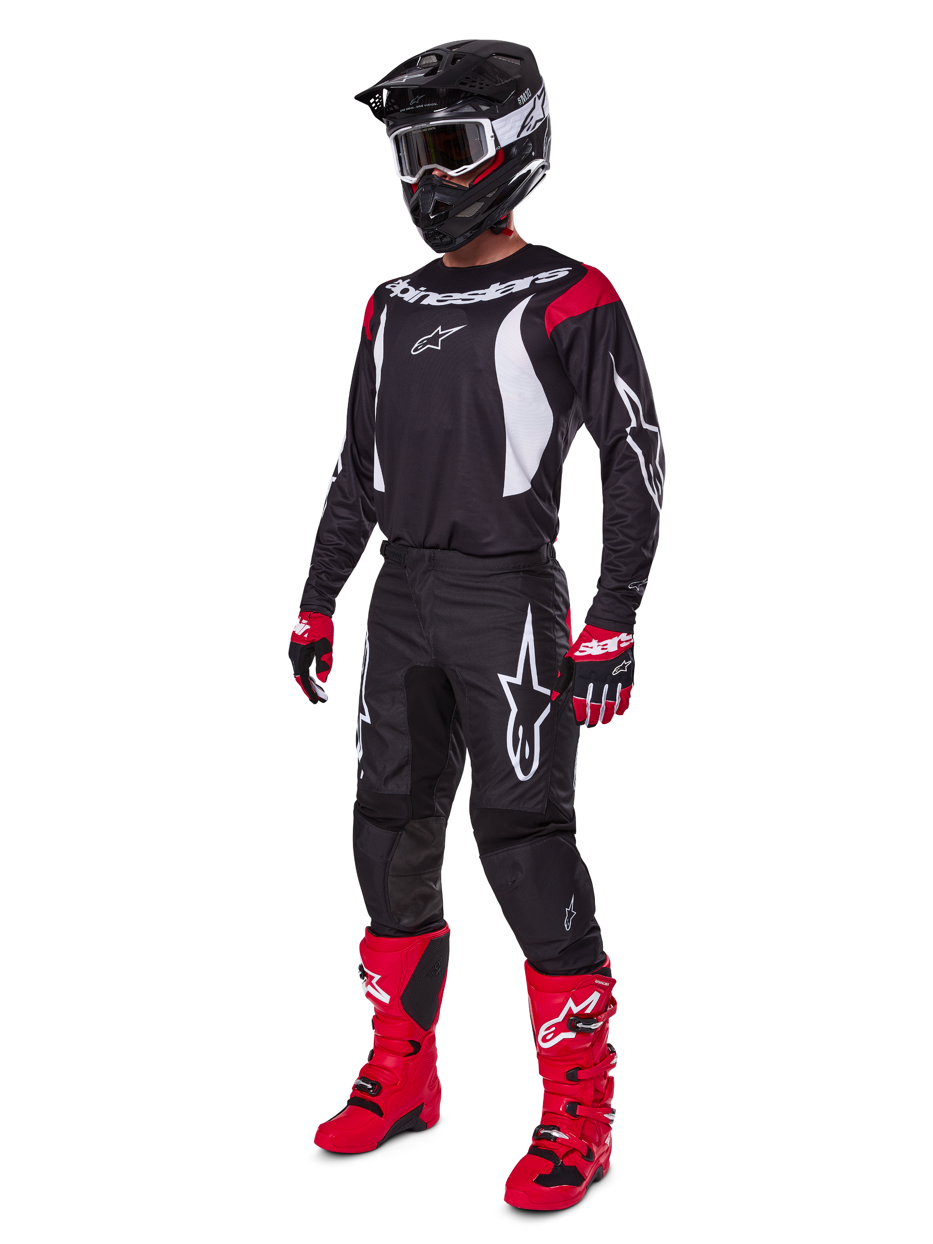Motocyklista motocrossowy w kompletnym zestawie Alpinestars 2025 Fluid Haul, czarna koszulka z czerwonymi i białymi akcentami, czarne spodnie z białym logo, jaskrawoczerwone buty, czerwono-czarne rękawice, czarny kask z goglami, dopasowany zestaw odzieży off-road