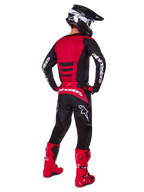 Zawodnik motocrossowy w zestawie Alpinestars 2025 Fluid Haul Gear Set, widok z tyłu, czerwono-czarna koszulka z białym brandingiem, pasujące czarne spodnie z czerwonymi akcentami, jaskrawoczerwone buty i czarny kask z białymi goglami, kompletny, dopasowany strój do wyścigów terenowych