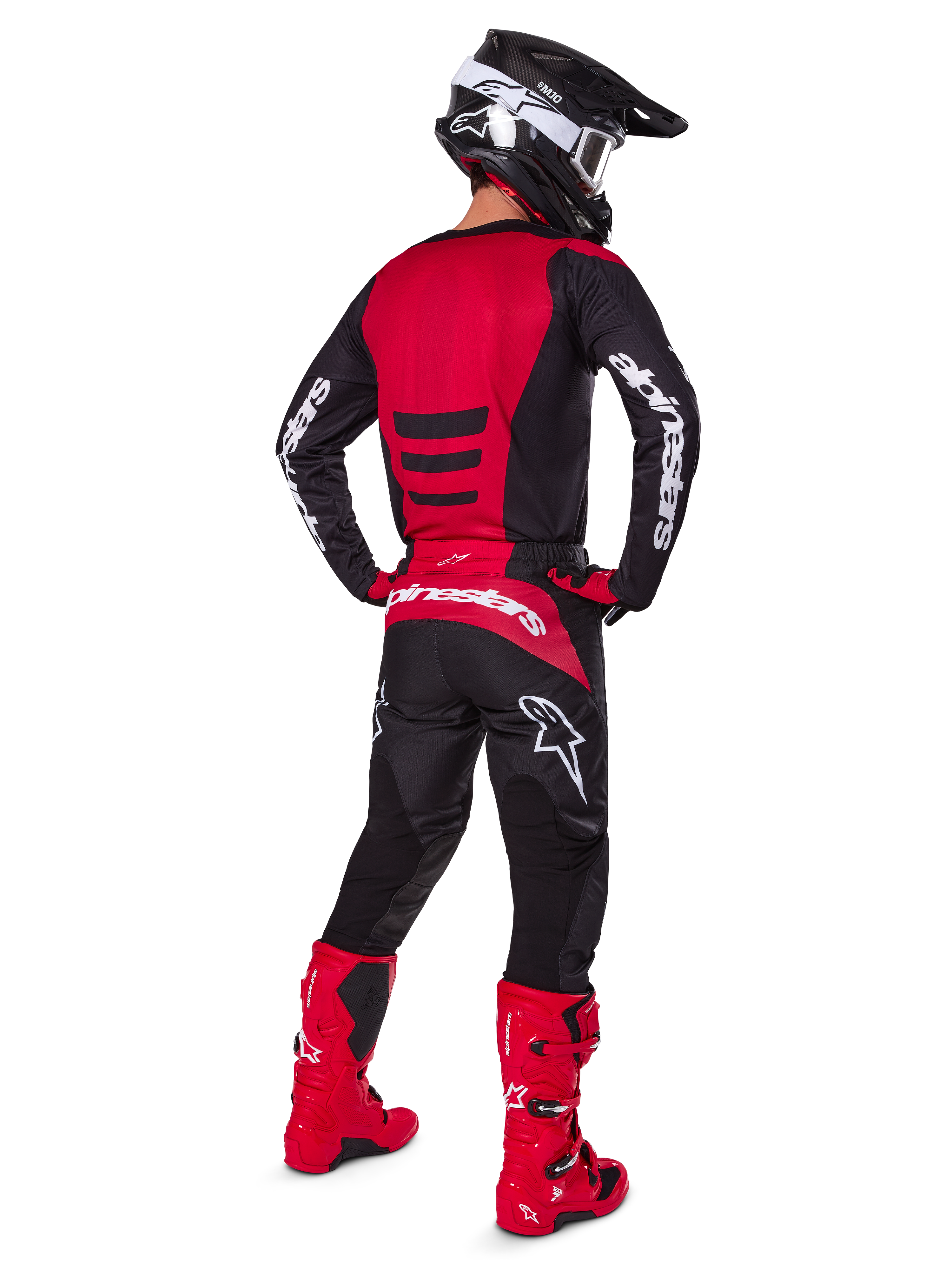 Zawodnik motocrossowy w zestawie Alpinestars 2025 Fluid Haul Gear Set, widok z tyłu, czerwono-czarna koszulka z białym brandingiem, pasujące czarne spodnie z czerwonymi akcentami, jaskrawoczerwone buty i czarny kask z białymi goglami, kompletny, dopasowany strój do wyścigów terenowych