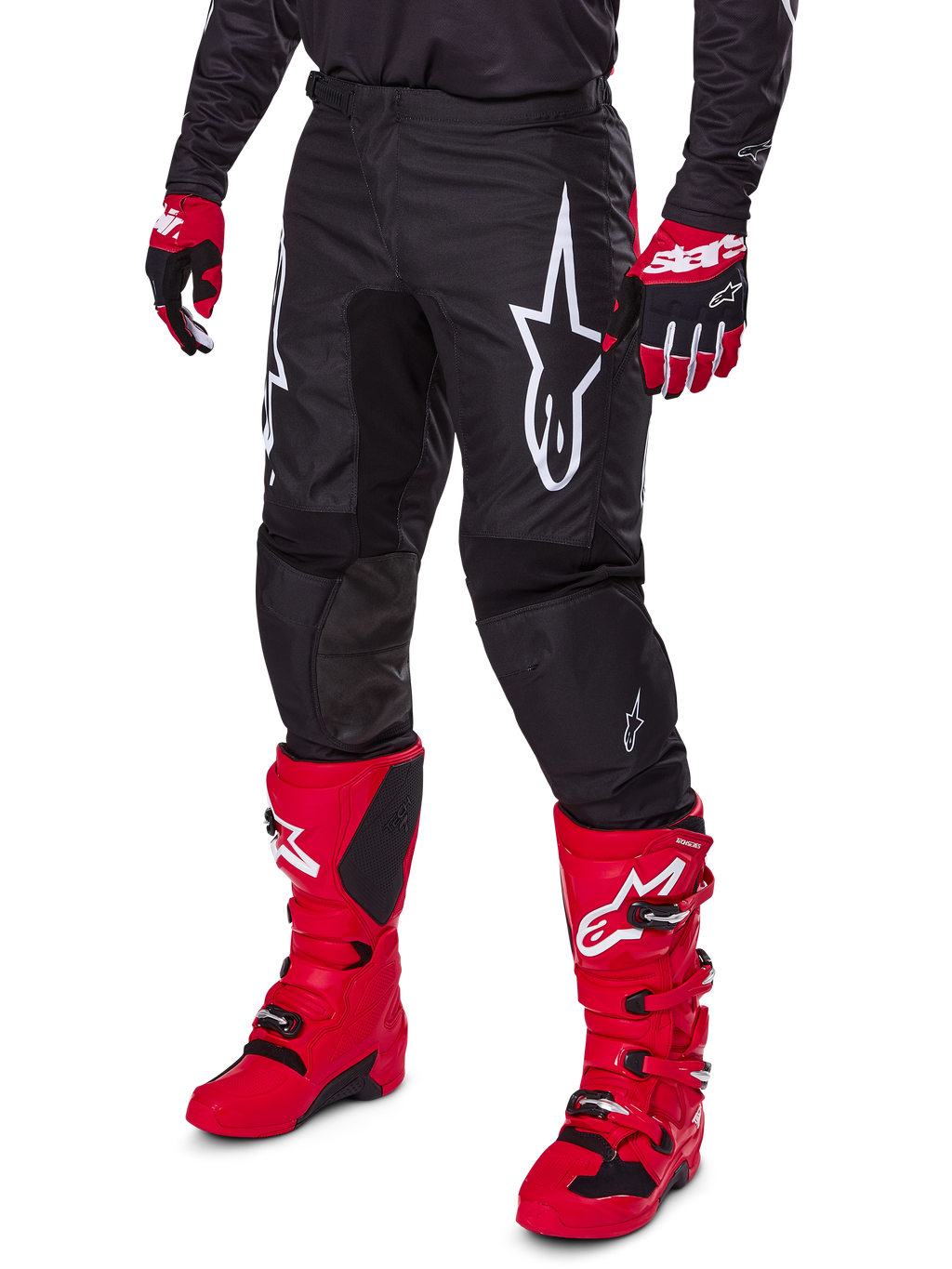 Alpinestars 2025 Fluid Haul Pants, spodnie motocrossowe, czarne z dużym białym logo Alpinestars, noszone z jaskrawoczerwonymi butami i czerwono-czarnymi rękawicami, wytrzymała konstrukcja z poliestru 600D o ergonomicznym kroju do jazdy terenowej