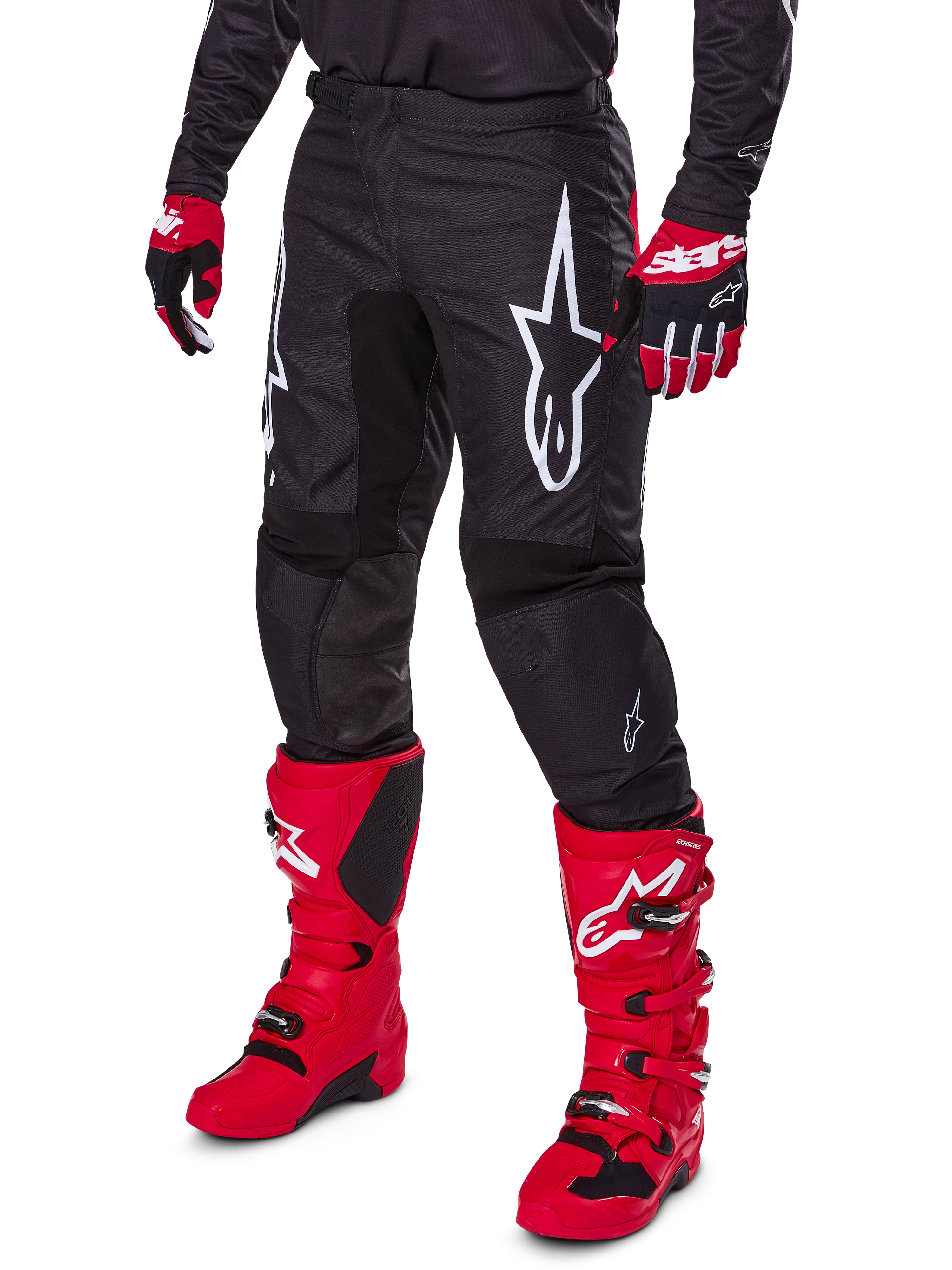 Alpinestars 2025 Fluid Haul Pants, spodnie motocrossowe, czarne z dużym białym logo Alpinestars, noszone z jaskrawoczerwonymi butami i czerwono-czarnymi rękawicami, wytrzymała konstrukcja z poliestru 600D o ergonomicznym kroju do jazdy terenowej