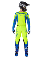 Alpinestars 2025 Fluid Haul Pants, spodnie motocrossowe, fluorescencyjny żółty i niebieski, noszone jako kompletny zestaw wyścigowy z pasującą koszulką, niebieskimi butami i czarnym kaskiem, z wyraźnym niebieskim brandingiem na udach i czarnymi panelami na kolanach