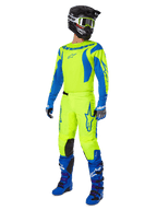 Alpinestars 2025 Fluid Haul Pants, spodnie motocrossowe, jaskrawożółty fluo i niebieski, noszone jako część pełnego zestawu wyścigowego z pasującą koszulką, niebieskimi butami i czarnym kaskiem, projekt o wysokiej widoczności do jazdy terenowej