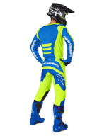Zawodnik motocrossowy widziany od tyłu w spodniach Alpinestars 2025 Fluid Haul i dopasowanej koszulce w kolorach żółtym fluo i niebieskim, w połączeniu z niebieskimi butami i czarnym kaskiem Alpinestars, profesjonalny strój do wyścigów terenowych