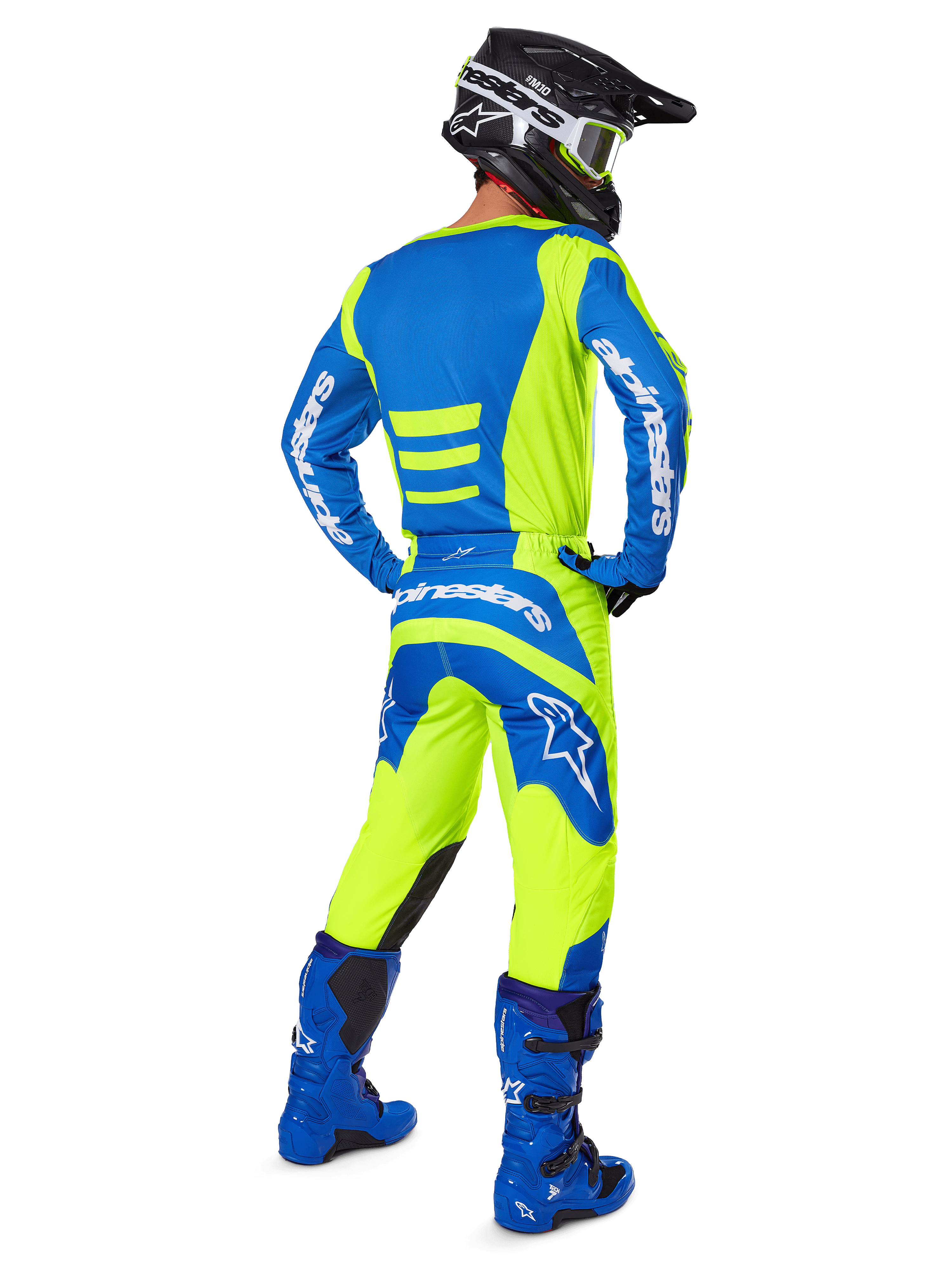 Zawodnik motocrossowy widziany od tyłu w spodniach Alpinestars 2025 Fluid Haul i dopasowanej koszulce w kolorach żółtym fluo i niebieskim, w połączeniu z niebieskimi butami i czarnym kaskiem Alpinestars, profesjonalny strój do wyścigów terenowych