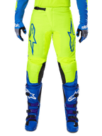 Alpinestars 2025 Fluid Haul Pants, spodnie motocrossowe, jaskrawo żółte i niebieskie, noszone z pasującymi rękawicami i butami, czarne panele wewnętrzne na kolanach, wyrazisty niebieski branding na udach, sportowy ergonomiczny design.