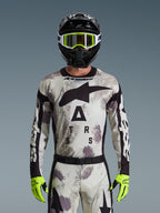 Alpinestars 2026 Racer Lahnd Jersey, zestaw motocrossowy, wzór Sand Camo w odcieniach szarości i bieli, duże czarne logo z gwiazdą i napis „ASTARS”, w zestawie z czarnym kaskiem, neonowożółtymi goglami i rękawicami, profesjonalny sprzęt wyścigowy off-road